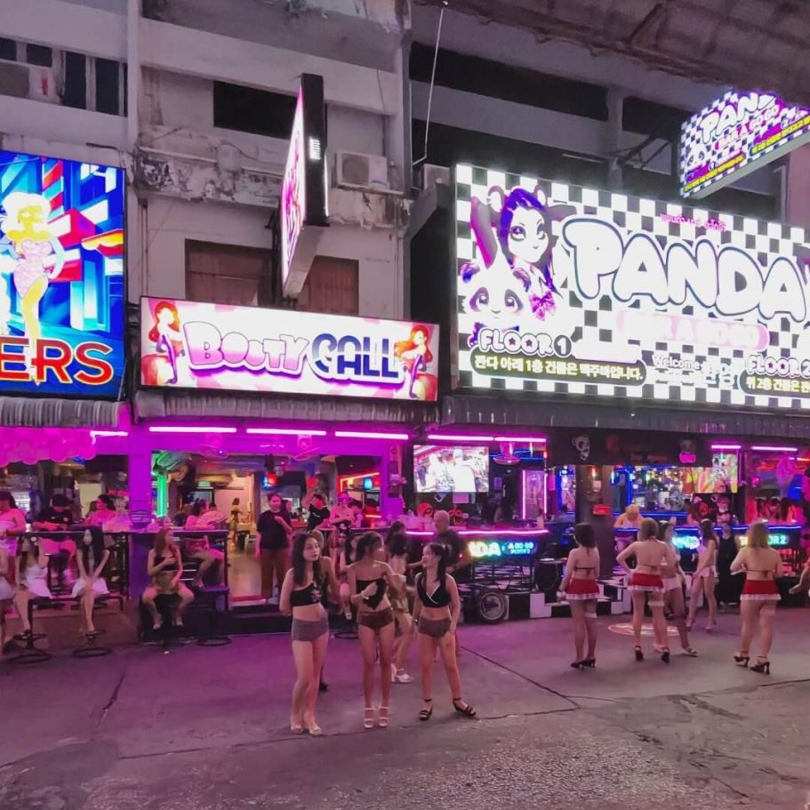 Nachtaufnahme der Soi 6 in Pattaya mit den leuchtenden Bars Booty Call und Panda. Frauen stehen auf der Straße.