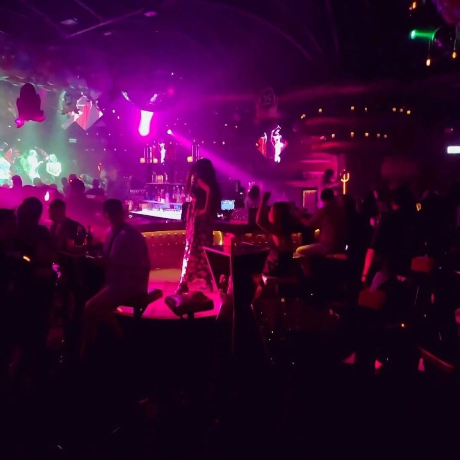 Innenansicht des Lucifer Club Pattaya bei Nacht - Gäste feiern an Tischen, bunte Lichter und Bühnennebel schaffen Club-Atmosphaere.