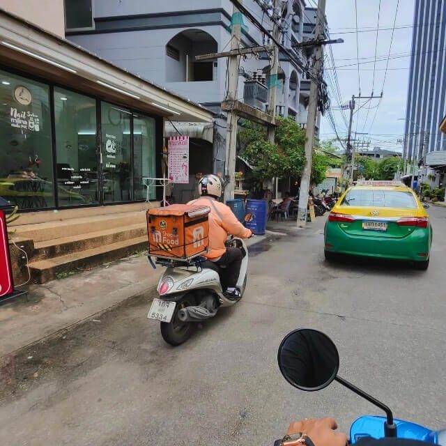 Lieferdienst und Verkehr in Pattaya Lieferfahrer auf dem Roller neben einem Taxi in Pattaya