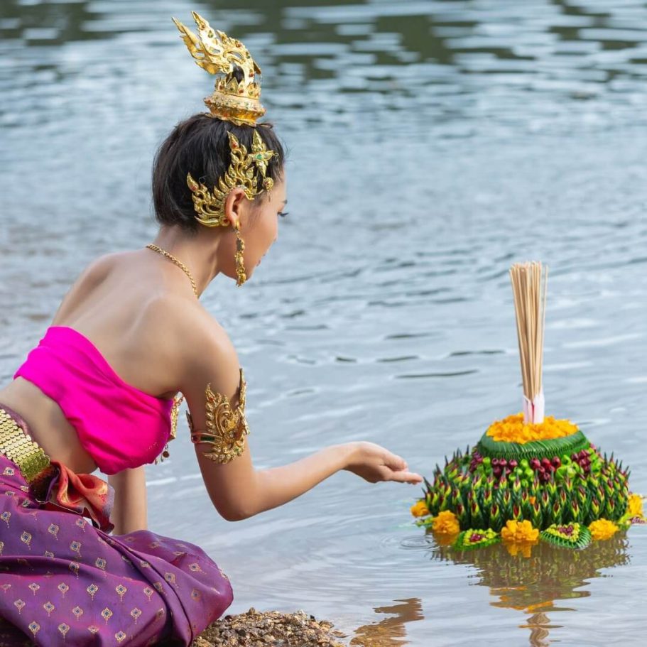 Loy Krathong – Zauberhafte Momente am Wasser erleben! Traditionell gekleidete Frau, die während des Loy Krathong Festes einen dekorierten Krathong ins Wasser setzt.