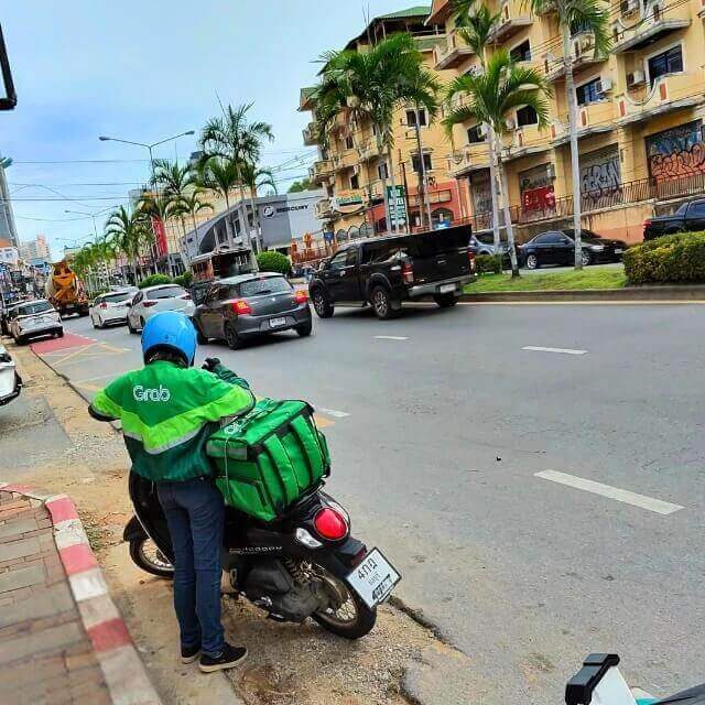 Grab Fahrerin fährt mit grüner Lieferbox durch eine Seitenstraße in Pattaya