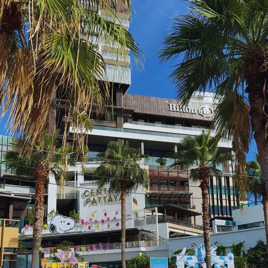Ansicht des modernen Hilton Hotel Pattaya Gebäudes mit markantem Logo, umgeben von tropischen Palmen unter klarem blauem Himmel