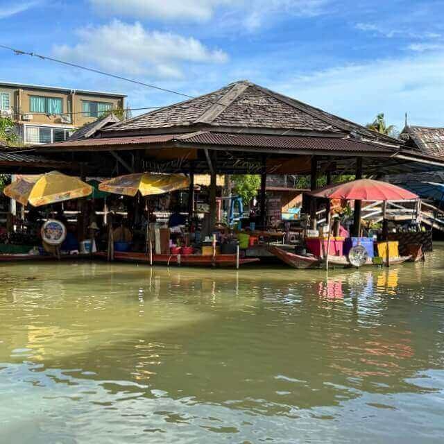 Pattaya Floating Market mit Marktstand am Wasser, Holzgebäude und Boot unter blauem Himmel