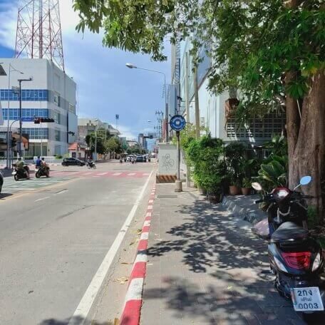 Straße in Pattaya mit Gehweg, Gebäuden, Bäumen und einem Roller am Straßenrand