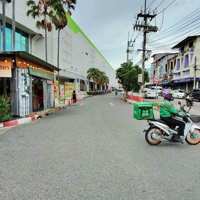 Grab Lieferfahrer mit grüner Lieferbox fährt vor dem Big C Extra in Pattaya