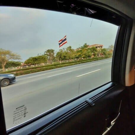 Taxifahrt nach Pattaya Blick aus einem fahrenden Taxi auf eine Straße in Thailand mit thailändischer Flagge