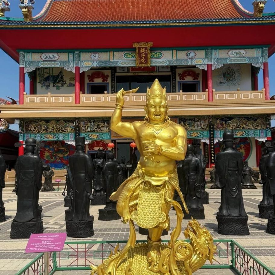 Kuixing-Statue im Viharn Sien Tempel Pattaya Goldene Statue des Kuixing mit erhobenem Arm, umgeben von dunklen Figuren im Hof des Viharn Sien Tempels in Süd-Pattaya