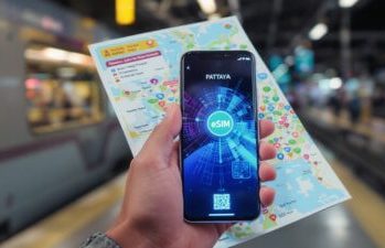 Eine Hand hält ein Smartphone und eine Karte an einem Bahnhof – digitale Reiseplanung in Thailand.