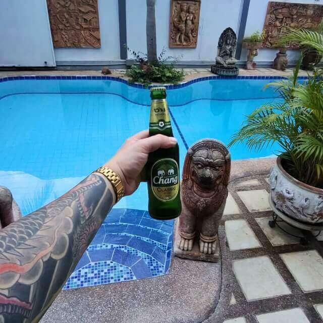 Nach dem Trinken besser Bolt rufen Hand mit Chang Bier an einem Pool in Pattaya mit thailändischer Dekoration im Hintergrund