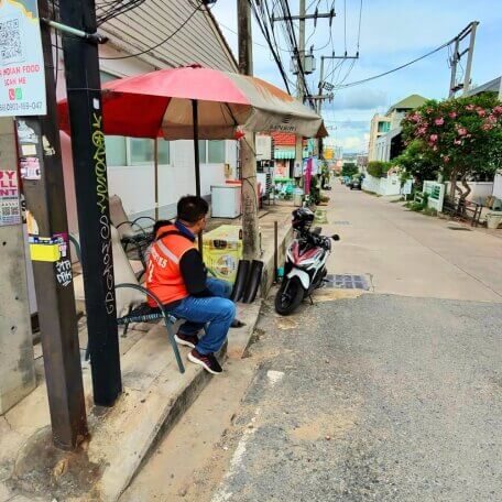Taxifahrer wartet am Straßenrand in Pattaya Taxifahrer sitzt neben einem Motorroller an einer kleinen Straße in Pattaya und wartet auf Kundschaft