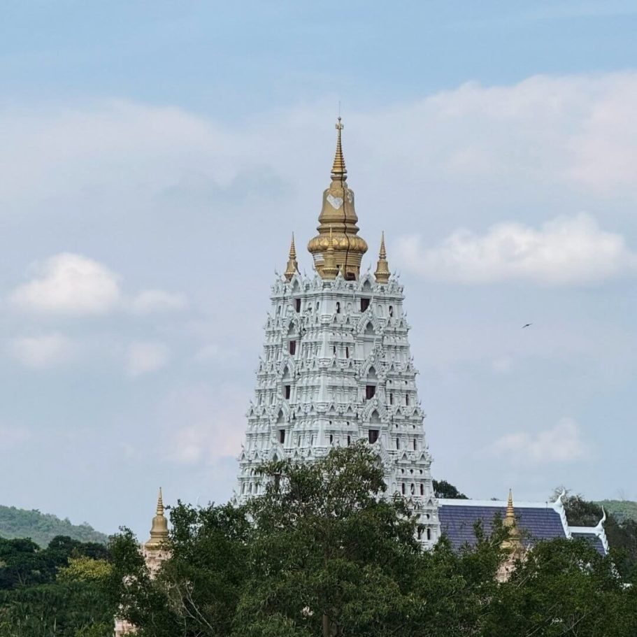Weißer Chedi mit goldener Spitze des Wat Yansangwararam, ragt über die Baumkronen vor blauem Himmel