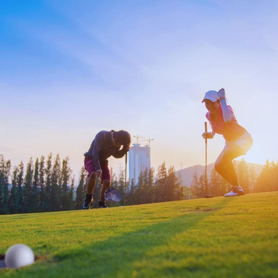 Zwei Golfspieler auf einem gepflegten Golfplatz in Pattaya, Thailand, bei Sonnenuntergang, mit moderner Skyline im Hintergrund.