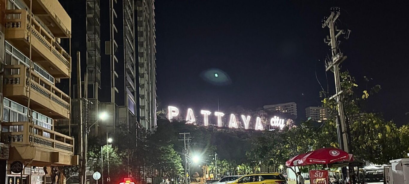 Nächtliche Straße in Pattaya mit beleuchtetem Pattaya City Sign, Gebäuden und Straßenverkehr