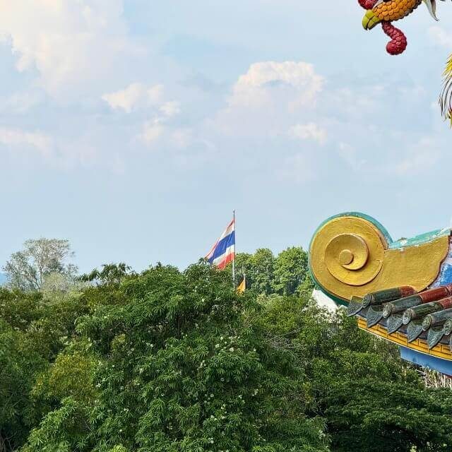 Thailändische Flagge und Tempelanlage zwischen Bäumen