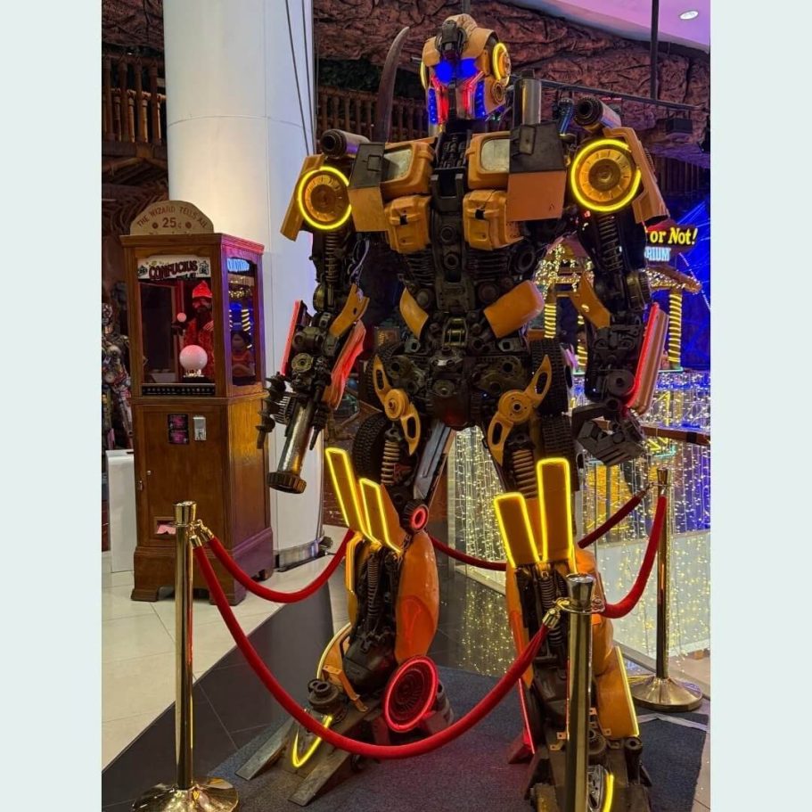 Imposante Transformers-ähnliche Roboterskulptur aus recycelten Autoteilen in goldenen und schwarzen Farbtönen