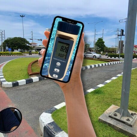 Smartphone mit Messgerät unterwegs in Pattaya Hand hält ein Smartphone mit digitalem Messgerät vor einer Straße in Pattaya