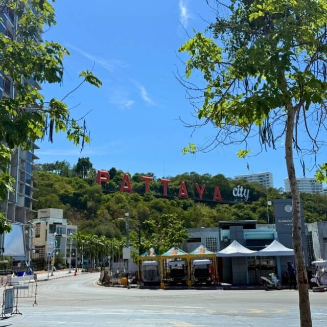Pattaya City bei sonnigem Wetter Pattaya City Schriftzug mit Straße, Bäumen und blauem Himmel