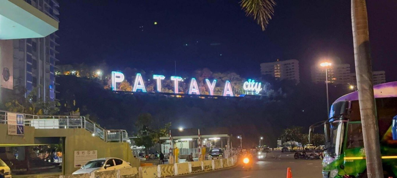 Pattaya City Schild bei Nacht mit Straße und Baht Bus
