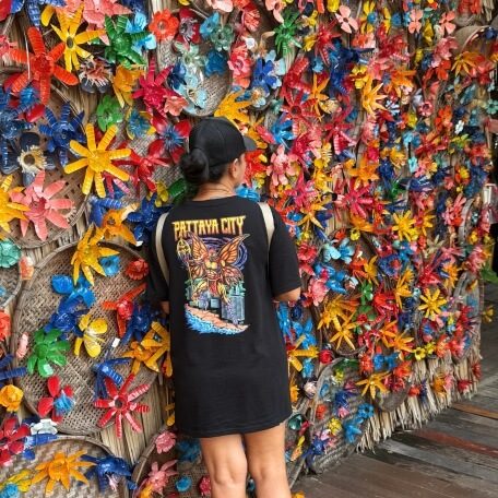 Person vor einer bunten Wand mit vielen farbigen Plastikblumen und Dekorationen