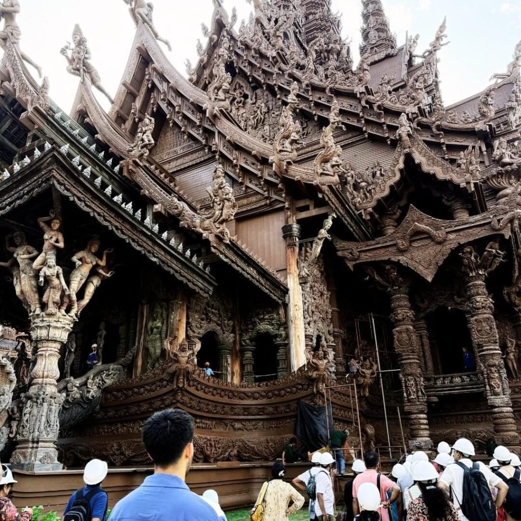 Besuchergruppe mit Helmen vor der kunstvoll geschnitzten Holzfassade des Sanctuary of Truth in Pattaya während einer geführten Tempeltour.